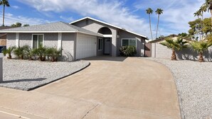 Une maison moderne de plain-pied, dotée d’un garage, d’une allée et d’un espace paysager agrémenté de palmiers et d’arbustes.