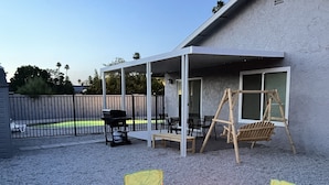 Une terrasse extérieure dotée d’un foyer, de quatre chaises pliantes vertes et d’un espace salon couvert avec une balançoire.