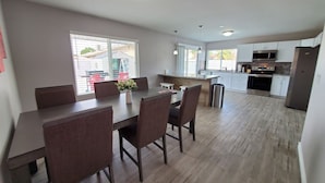 Une cuisine moderne avec des meubles blancs, des appareils en acier inoxydable et un coin repas comprenant une table et des chaises en bois.