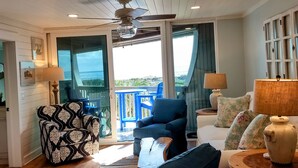 A spacious living area with a wooden ceiling, a large window offering a view of the outdoors, a sofa, a chair, and a table with a vase.
