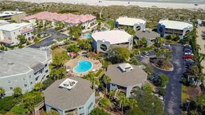 An aerial view of a resort with multiple buildings, a swimming pool, and a beach in the background.