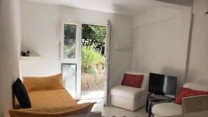 Une chambre moderne avec un lit, une chaise, un téléviseur et une fenêtre donnant sur un jardin.