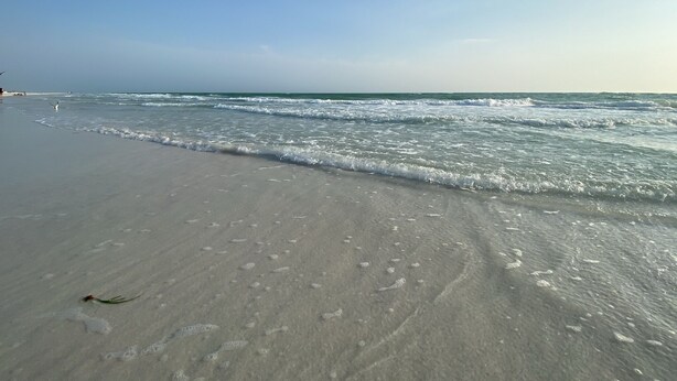 Een strand met heldere lucht, zachte golven en een zandstrand.