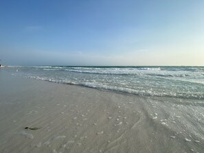 A beach with clear skies, gentle waves, and a sandy shore.