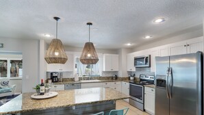 Een moderne keuken met een groot eiland, roestvrijstalen apparatuur en lichtblauwe barkrukken.
