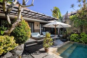 Un espace piscine extérieur moderne, doté de chaises longues, d’une pergola et de plantes tropicales.