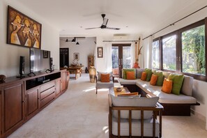 Un salón espacioso con sofá, mesa de centro y televisor. Incluye un ventilador de techo, comedor y ventanas amplias.