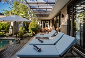 A poolside area with lounge chairs, a covered patio, and a dining area, and a view of the pool.