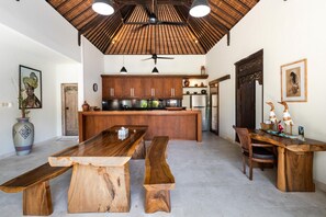 Una cocina con armarios de madera, una isla central y un comedor con mesas de madera rústica.