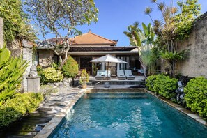 A swimming pool with lounge chairs, a pergola, and tropical plants.