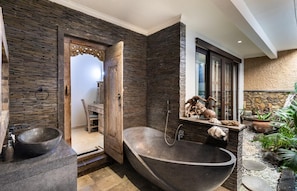 Une salle de bain avec un mur en pierre, une porte en bois, une baignoire et une fenêtre donnant sur un beau paysage.