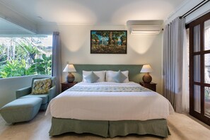 Une chambre d’hôtel avec un grand lit, deux tables de chevet avec des lampes, un fauteuil à revêtement vert et une grande fenêtre donnant sur un paysage verdoyant.