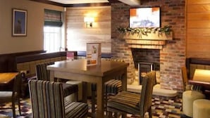 A cozy lobby with a brick fireplace, striped chairs, a wooden table, and a checkered floor. - Premier Inn Lymington (Lymington)