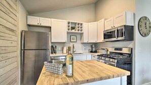 Una cocina moderna con armarios blancos, un refrigerador de acero inoxidable, una encimera de madera, una botella de vino y un reloj en la pared.