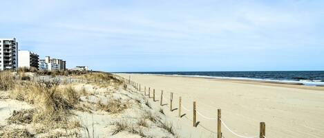 A sandy beach with a wooden fence and a row of buildings in the background.