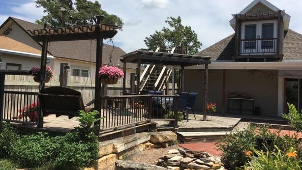 A residential backyard with a wooden pergola, a barbecue area, and a stone pathway. - The Monroe House (Great Bend)
