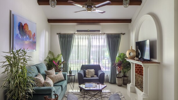 Un salon comprenant un canapé, un fauteuil, une table basse et un téléviseur. On y trouve également des plantes en pot et un ventilateur de plafond.