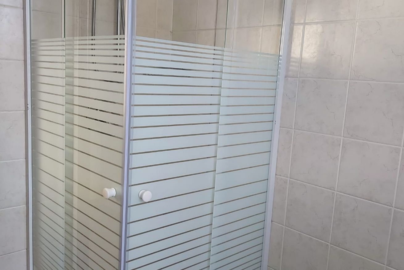 A glass-enclosed shower stall with horizontal blinds, white tiled walls, and a visible door handle.
