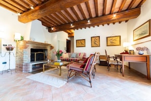 Un salon chaleureux avec une cheminée, des poutres en bois, un canapé, des fauteuils et des œuvres d’art accrochées aux murs.