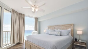 Un dormitorio con una cama grande, una mesita de noche, un ventilador de techo y vista al océano.