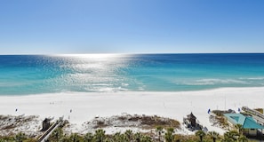 Ein Strand mit blauem Himmel, sandigem Ufer und einigen Gebäuden, darunter ein kleines Haus und ein Gazebo.