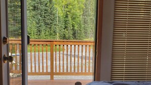 A bedroom with a large window, a wooden bed, and a view of a deck and forest. - The Lodge at Coliseum Mountain Resort (Clearwater County)