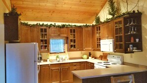 A kitchen with wooden cabinets, a refrigerator, a stove, and a window with blinds. - The Lodge at Coliseum Mountain Resort (Clearwater County)