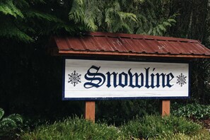 Ein hölzernes Schild mit der Aufschrift "Snowline" und Schneeflocken-Verzierungen, vor sattgrüner Vegetation.
