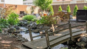 A wooden bridge over a stream in a landscaped garden with various plants and a wooden fence in the background. - Bryant Creek Escape-Minutes from downtown (Walla Walla)