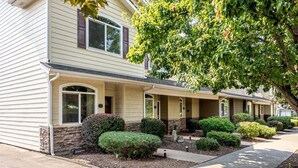 A row of townhouses with a stone foundation, a covered front porch, and a well-maintained front yard with hedges and a tree. - Bryant Creek Escape-Minutes from downtown (Walla Walla)