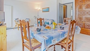 A dining area with a table set for four, surrounded by wooden chairs. There is a painting on the wall, a wooden cabinet, and a door with intricate carvings. - Le Grand Large by Interhome (Quiberon)