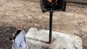 Ein Grill mit Flammen, einer Betonplatte und eine Tüte Holzkohle.