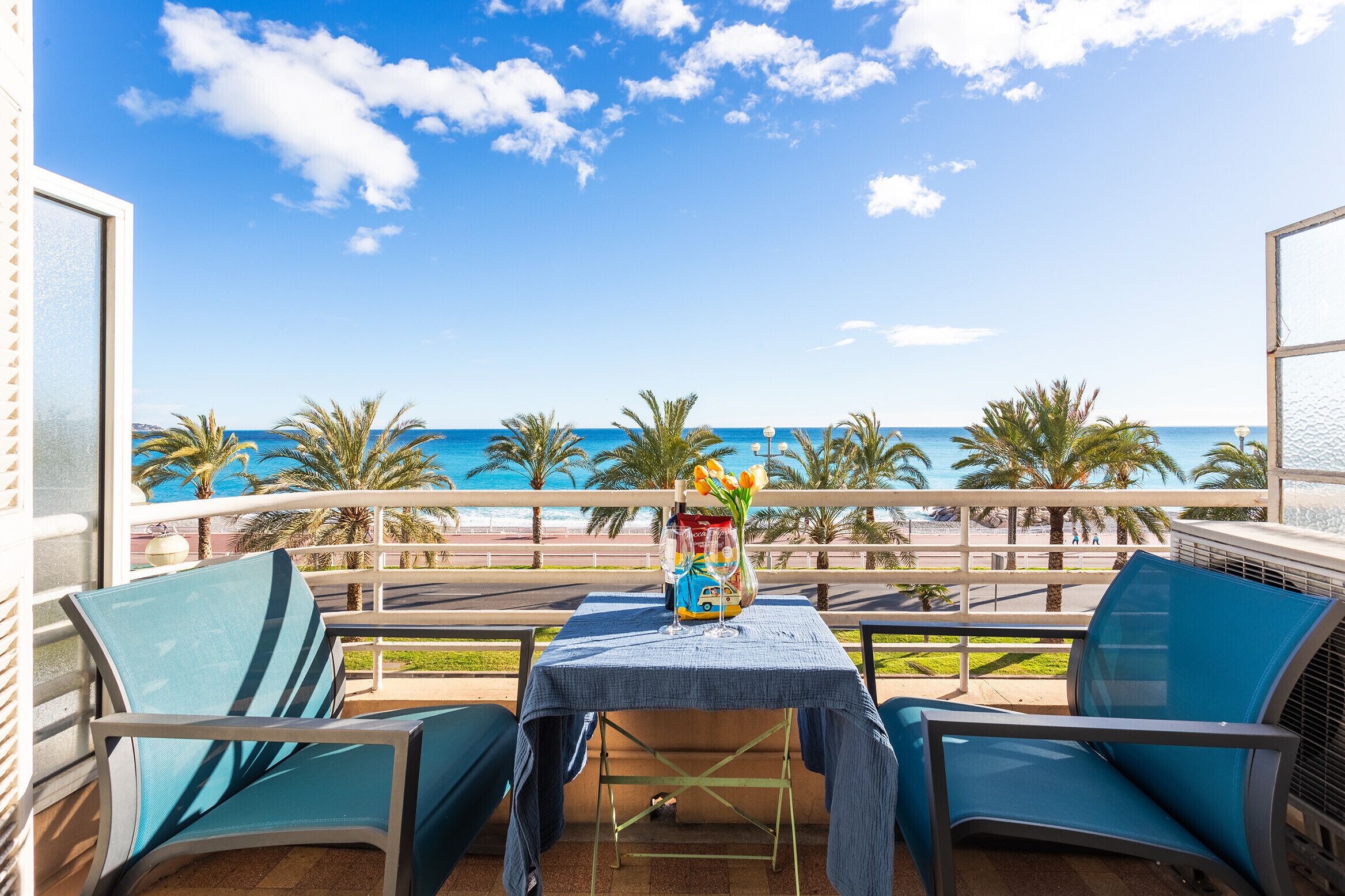 Ein Balkon mit Tisch für zwei Personen, mit Blick auf einen Strand mit Palmen und das Meer.