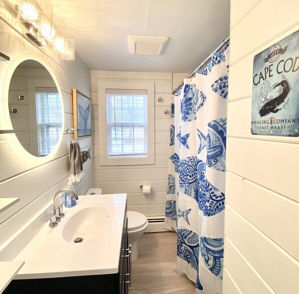Un baño con lavamanos, espejo, inodoro y cortina de ducha con un diseño azul y blanco.