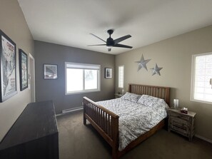 A bedroom with a bed, a dresser, a ceiling fan, and two windows.
