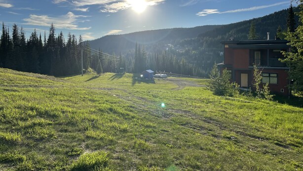 A grassy field with a building and a mountain in the background. - Ski in/ski out chalet. Mountain + valley views. Close to village. (Silver Star)