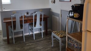 Een kleine keuken met een eettafel, stoelen, een magnetron, een koffiezetapparaat en een koelkast.