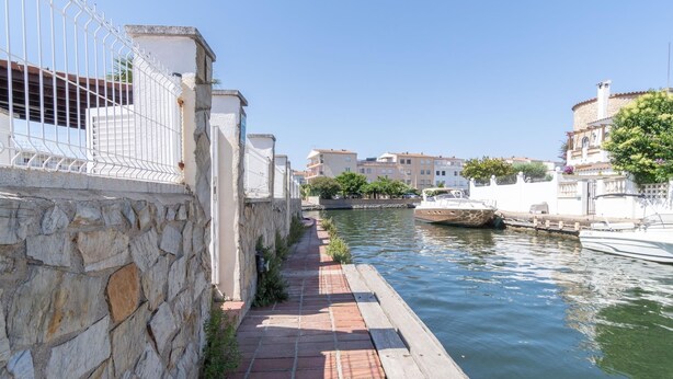 A narrow waterway with a stone wall on one side and a wooden dock extending into the water. - Casa de 4 habitaciones, 2 baños, piscina privada, amarre, wifi (Empuriabrava)