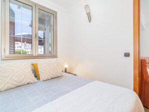 A bedroom with a bed, a window, a wall-mounted light, and a door.