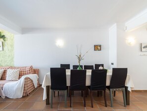 A dining area with a table set for six, surrounded by chairs, a sofa, and a wall-mounted light fixture.
