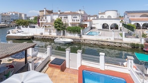 A waterfront property with a swimming pool, boats docked nearby, and Mediterranean-style architecture.
