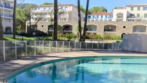 Una piscina con una cerca blanca, rodeada de edificios con balcones y un muro de piedra.