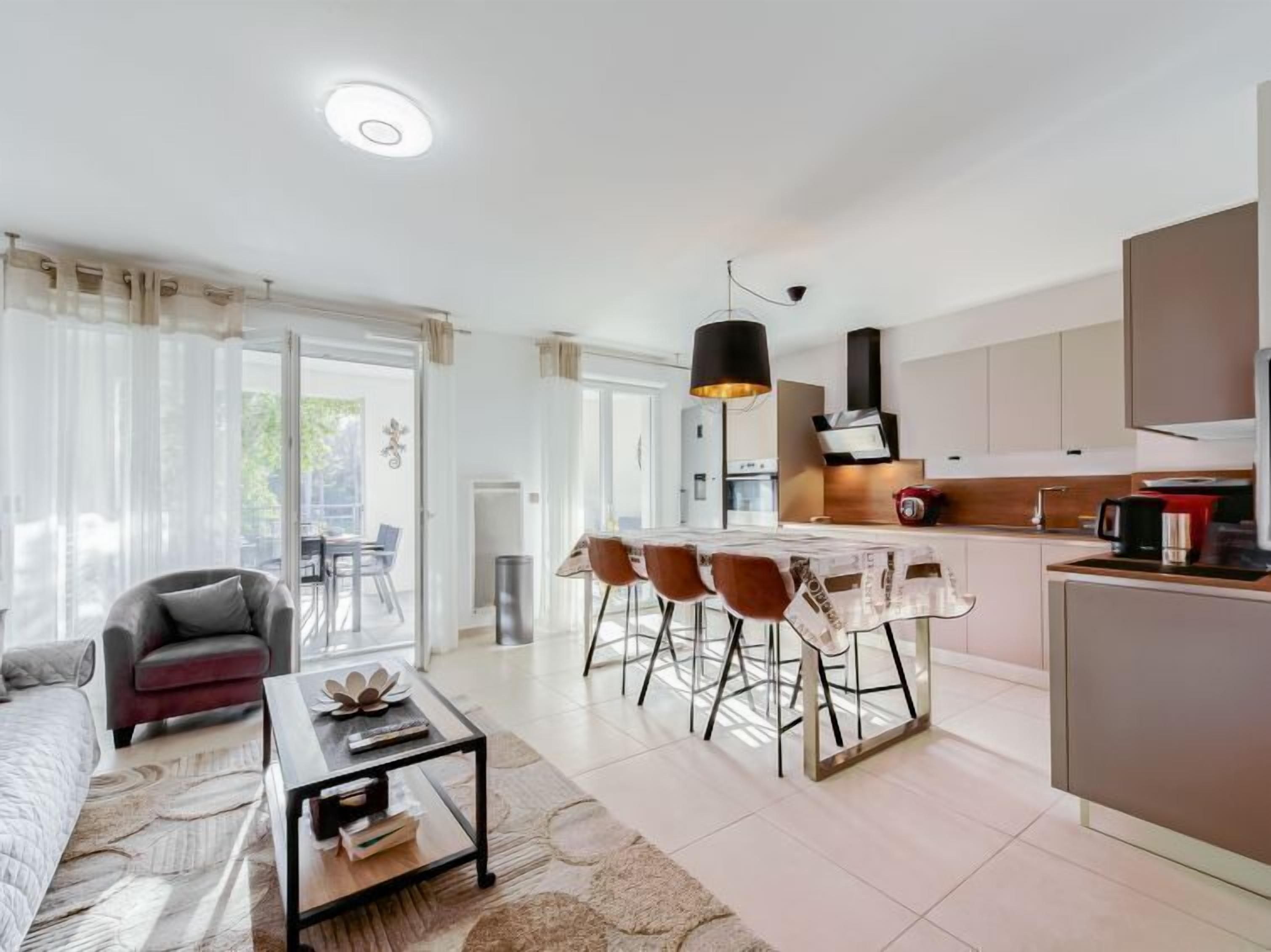 A modern living room with a sofa, coffee table, and dining area with chairs. There is a kitchen with cabinets and a dining table.