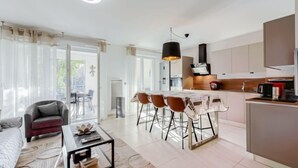 Una sala moderna con sofá, mesa de centro y comedor con sillas. Se observa una cocina con alacenas y una mesa de comedor.