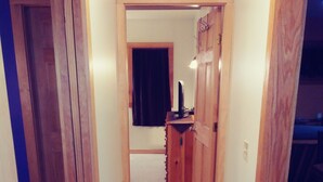 A narrow hallway with wooden doors and a carpeted floor, leading to a room with a desk and a chair. - Comfortable retreat in the woods, but close to Island attractions (Mount Desert)