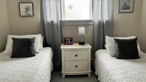 Quarto com duas camas, uma mesa de cabeceira com relógio e uma janela com cortinas.