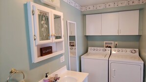 Uma lavanderia compacta com máquina de lavar e secadora, pia e espelho com moldura decorativa.