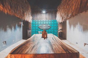 A room with a large wooden table, a blue patterned wall, and a thatched ceiling. - Kokohau Bungalows - Adults Only (Juan de Acosta)