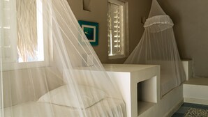 A bedroom with a bed under a mosquito net, a window with shutters, and a small bedside table. - Kokohau Bungalows - Adults Only (Juan de Acosta)