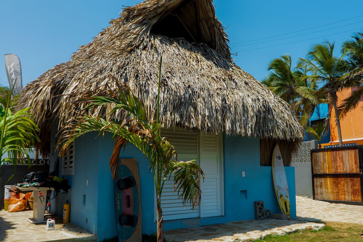 Une maison à toit de chaume, avec une façade bleue, une porte et un petit porche.